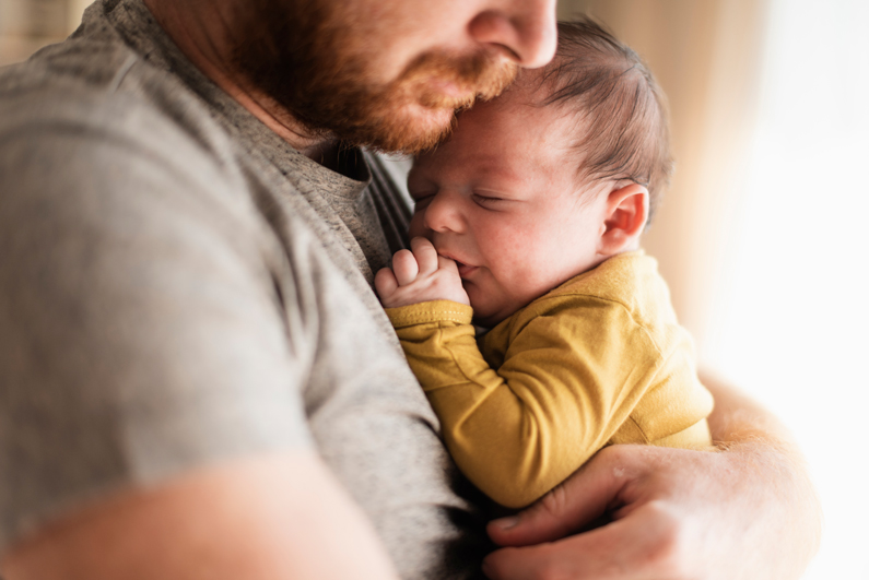 Vater in Eltern-Karenz hält sein neugeborenes Kind